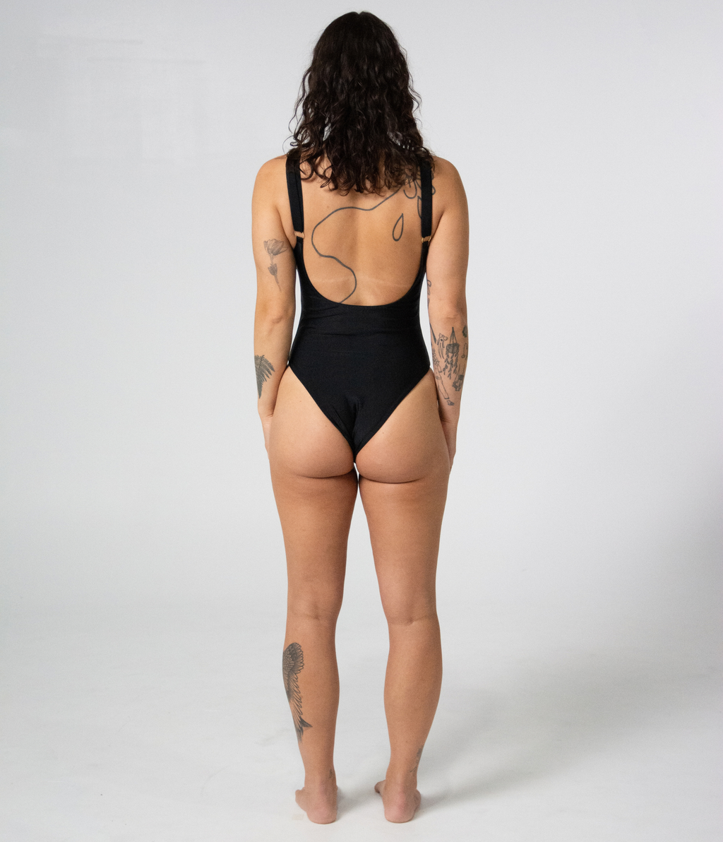 Mali One Piece in Noir (black), back view on model showing the scoop back and gold strap hardware