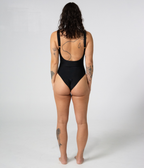 Mali One Piece in Noir (black), back view on model showing the scoop back and gold strap hardware