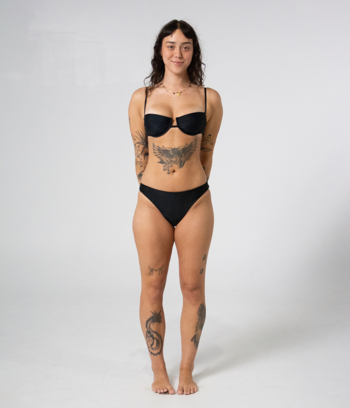 Wategos Underwire Top in Noir (black) worn with the Byron Low Rise Bottoms, front view on model with hands behind back