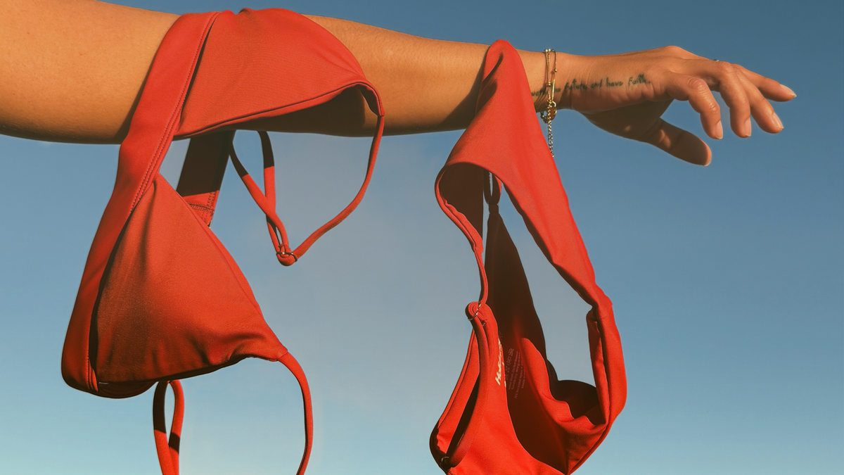 Kirra Triangle Top and Currumbin Bottoms in Rust, hanging from an outstretched arm against a clear blue sky